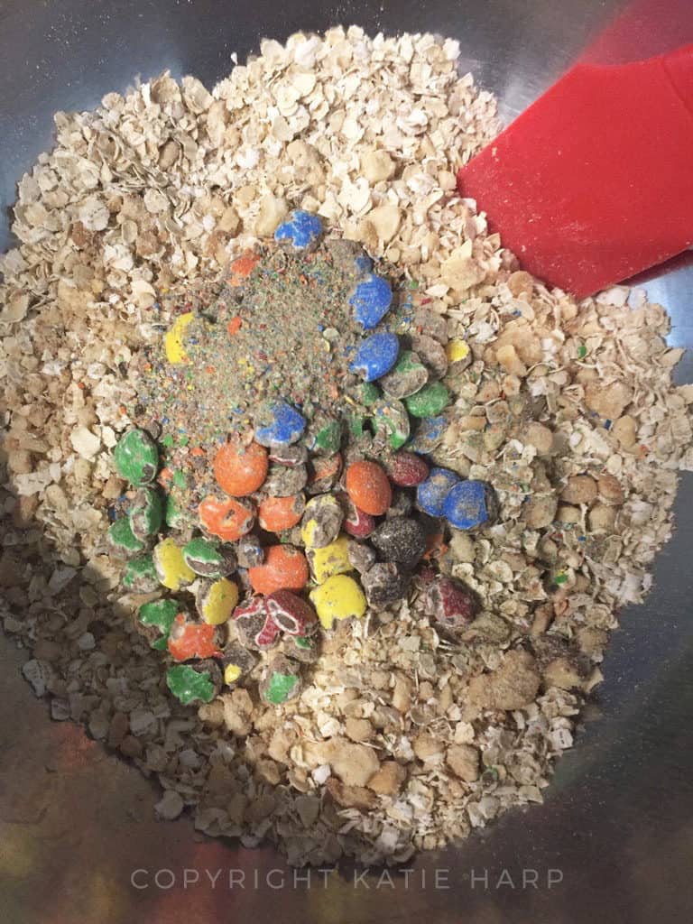 Adding M&Ms to the bowl of oats and nuts