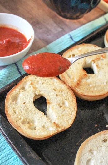 Spooning pizza sauce onto the bagels